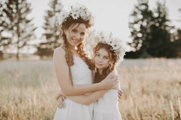 Fototapeta na wymiar happy sisters in white dresses with floral wreaths and boho style braids in summer in a field