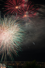 fireworks against a black sky background over a river and a bridge.