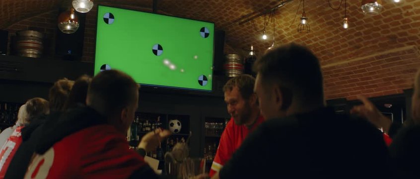 HANDHELD Model released, fans watching a game on a large TV in a sport pub, goal celebration, green screen chroma key with tracking points. Shot on ARRI Alexa Mini with Atlas Orion 2x Anamorphic lens