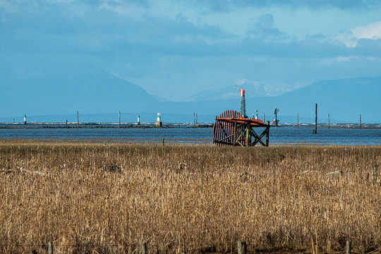 a broken orange windmill on the edge of brown grasses field wet land by the cost under blue sky