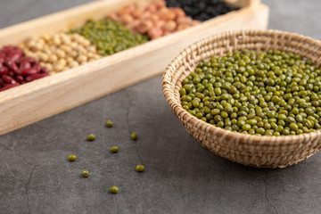 Green beans and grains in the wooden basket and in the wooden tray placed on the black cement floor. High angle view.