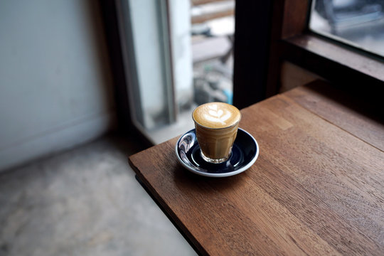 Hot Piccolo Latte - A glass of coffee with milk and beautiful leaf pattern latte art on wooden table and copy space, Perfect for breakfast time.