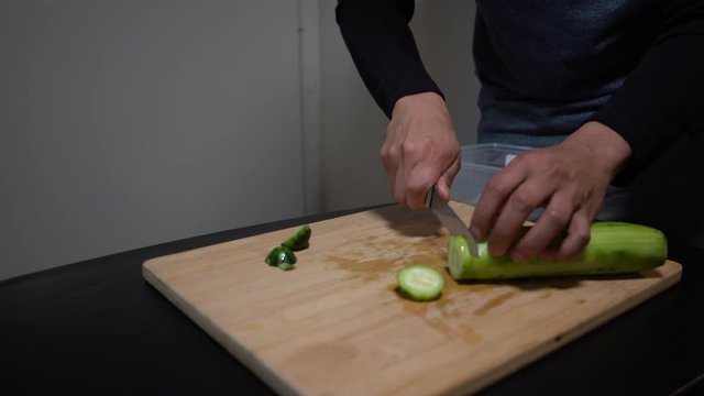 Chopping a cucumber on wooden chopping board