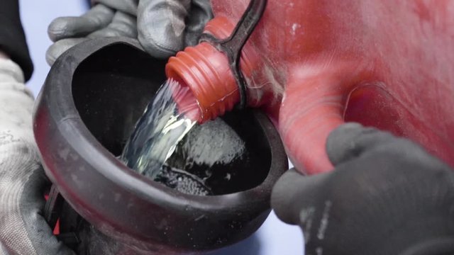 Pouring fuel gas into the tank of race car from fuel pot by two men mechanics in slow motion