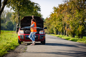 Pretty young woman by the roadside after her car has broken down, calling assistence, transportation concept