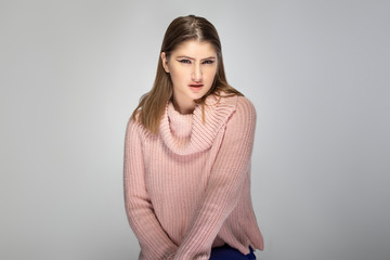 Close up portrait of a young Caucasian woman wearing a pink sweater on a grey background.  She...