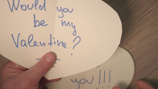 Man's hands hold several heart shaped cards from stranger with romantic writings. Up view and close up.