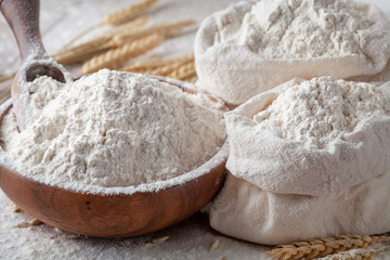 Fototapeta na wymiar Wheat flour in wooden bowl and burlap bag on kitchen table. Ingredient for baking.