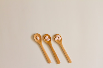 Assorted pharmaceutical medicine. Dosage. Tablets and capsules on a wooden spoon on a white background. Concept of medicine. Alternative homeopathy. Flatley.   copyright of the text.
