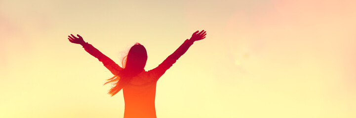 Happy woman sihouette with arms raised up in success on sunset glow sunshine banner panorama. Wellness, financial freedom, healthy life concept background.