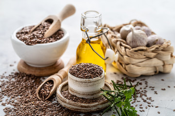 Flaxseed oil in a bottle and ceramic bowl with brown flax seeds and wooden spoon on a white background