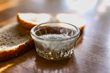Two pieces of black bran fresh bread with white salt in a salt shaker, standing on a wooden brown table in the sunlight.