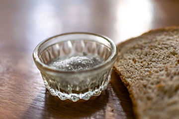 Two pieces of black bran fresh bread with white salt in a salt shaker, standing on a wooden brown table in the sunlight.