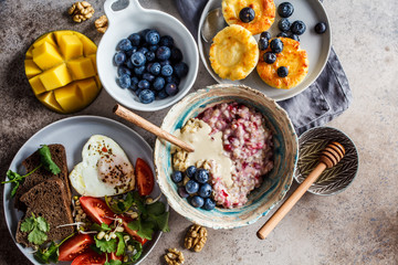Breakfast flat lay. Oatmeal, cottage cheese pancakes with berries and fried egg with salad on dark background.