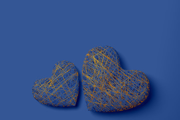 Two handmade hearts woven from a variety of blue and gold threads lie on a black background with a copy of space. 3D illustration