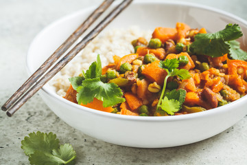 Vegan curry with rice in white bowl. Curry with sweet potato, peas and beans in a plate with rice.