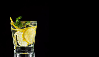 Cold drink on a black background. One glass with lemonade or mojito cocktail with lemon and mint. Copy space, close up.
