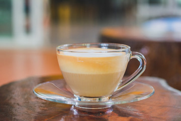 Layer of hot cappuccino coffee and milk froth in clear cup on wooden table in coffee shop.