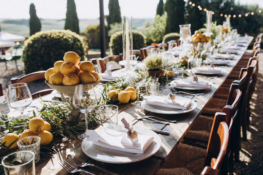 in the back yard of the old villa there is a long festive table, which is decorated with lemons and herbs, on the table are plates, glasses and candles. Wedding in Italy. Tuscany