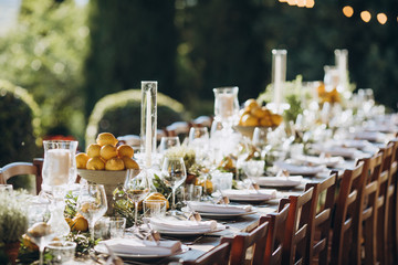 in the back yard of the old villa there is a long festive table, which is decorated with lemons and herbs, on the table are plates, glasses and candles. Wedding in Italy. Tuscany