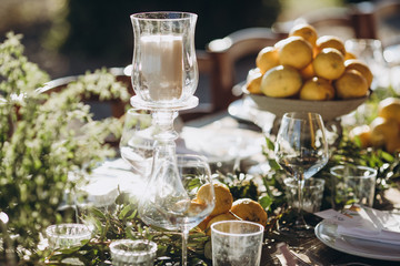 in the back yard of the old villa there is a long festive table, which is decorated with lemons and herbs, on the table are plates, glasses and candles. Wedding in Italy. Tuscany