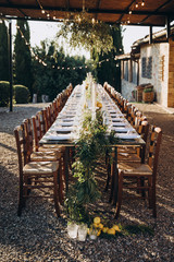 in the back yard of the old villa there is a long festive table, which is decorated with lemons and herbs, on the table are plates, glasses and candles. Wedding in Italy. Tuscany