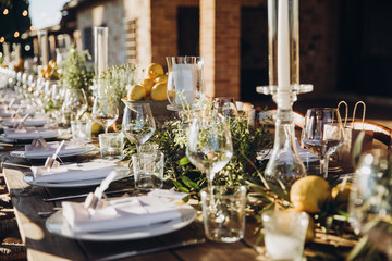 in the back yard of the old villa there is a long festive table, which is decorated with lemons and herbs, on the table are plates, glasses and candles. Wedding in Italy. Tuscany