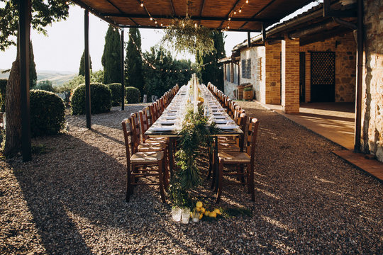 in the back yard of the old villa there is a long festive table, which is decorated with lemons and herbs, on the table are plates, glasses and candles. Wedding in Italy. Tuscany