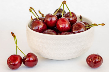 ripe red garden cherries with stems on a white bowl close up, white background, still life
