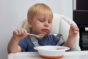 Three year old boy eats from a plate with a spoon