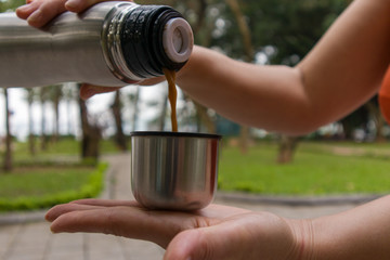 Woman pours a drink from a thermos holding it in her hands while standing in a park
