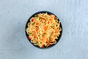 Instant noodles with carrot, scallions, and a sauce, a vegetable soba bowl, shot from the top on a slate background