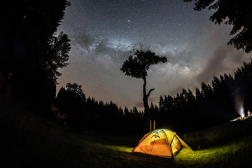 Milky Way and tree on the Beskydy mountains in Czech Republic with glowing tent.