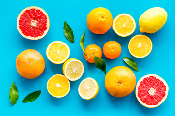 Fresh citrus background. Oranges, grapefruits, leaves - whole fruits and halfs - on blue background top-down