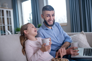 Dad and daughter with tea and cookies sitting on the couch.