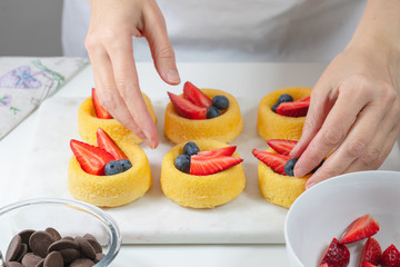 Biscuit cakes with fresh berries, chocolate, and whipped heavy cream. Fresh mini biscuit cups close up on white background, woman hands