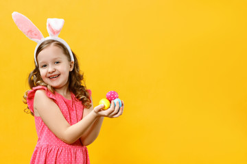 Happy little girl holding easter eggs in her hands. Close-up portrait of a child on a yellow background. Copy space
