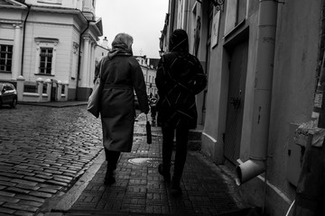 Two girls/tourists strolling around town with old architecture, on black and white background