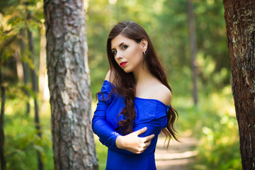 Portrait of a beautiful, young girl in a blue dress against a forest background.