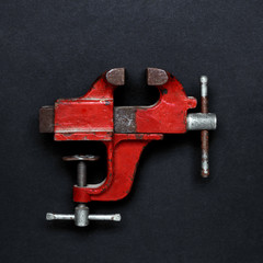 Vintage mechanical hand vise clamp red color on on grey background, top view. Creative design idea - obrazy, fototapety, plakaty