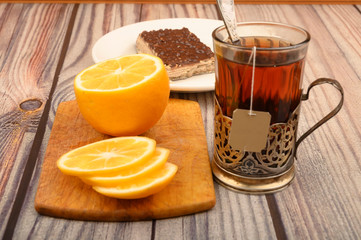 Tea in a faceted glass in a vintage Cup holder, sliced lemon on a Board and a piece of waffle cake on a white plate on a wooden background. Close up.