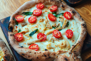 Freshly baked pizza with cheese, sauce, basil and tomato on a wooden table close up