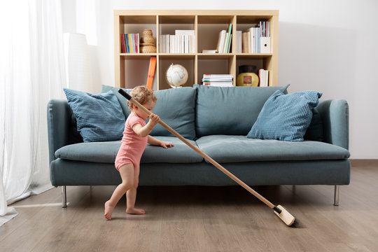Young toddler sweeping living room floor with broom