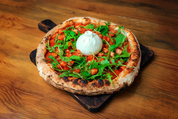 Freshly baked pizza with cheese, arugula, and burrata on a wooden table