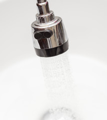 Water tap faucet with flowing water in a white bathroom sink.