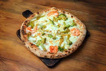 Freshly baked pizza with cheese, sauce, shrimps and broccoli on a wooden table