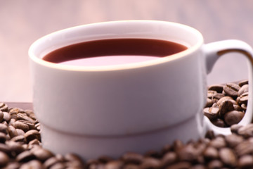 Coffee cup in white colour with dark coffee and coffee beans. This is on a wooden surface