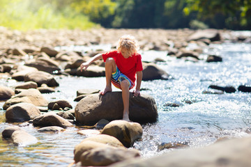 Child hiking in mountains. Kids at river shore.
