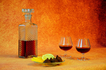 Crystal decanter with cognac and two glasses of drink next to a plate with appetizers, cut lemon...