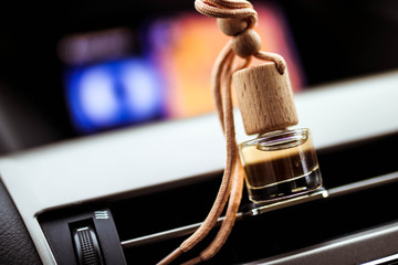Car air perfume freshener bottle inside the car on car panel. Aromatic liquid in the small bottle.